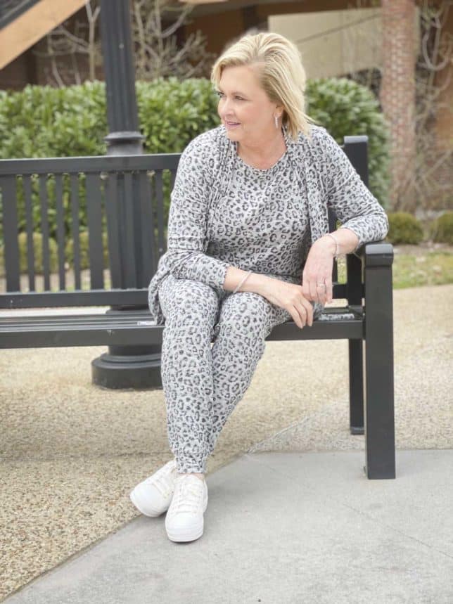 Fashion Blogger 50 Is Not Old is sitting on a black bench and wearing animal print loungewear from Chico's and Ked's platform sneakers