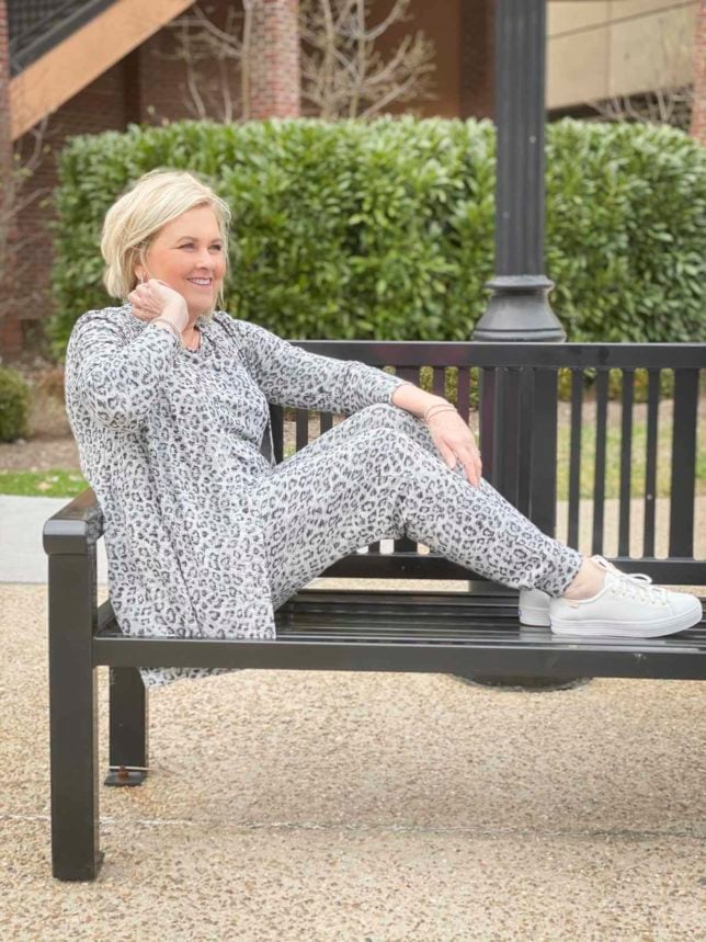 Fashion Blogger 50 Is Not Old is sitting with her feet on a bench and wearing animal print luxe loungewear from Chico's and Ked's platform sneakers