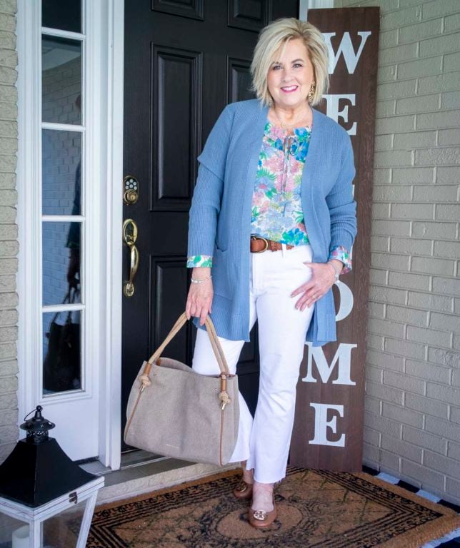 Fashion Blogger 50 Is Not Old is wearing white cropped jeans with a floral top, a long blue cardigan, and Tory Burch ballet flats