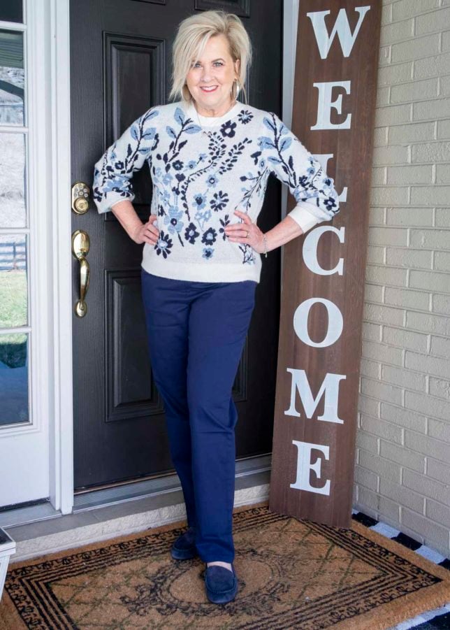 Fashion Blogger 50 Is Not Old is wearing a white sweater with a blue floral pattern, navy chino pants, and navy suede loafers