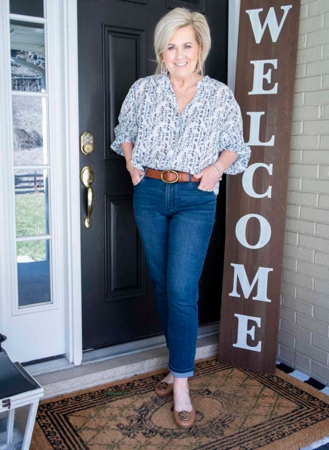 Fashion Blogger 50 Is Not Old is wearing a white blouse with a blue floral vine pattern, girlfriend jeans, and brown Tory Burch loafers
