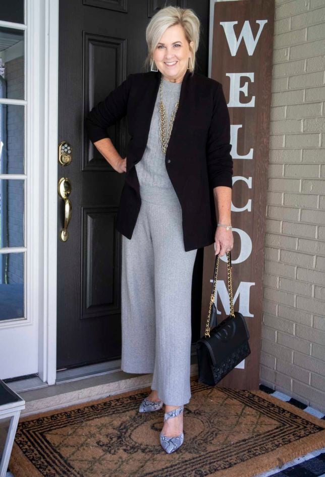 Fashion Blogger 50 Is Not Old is wearing a black blazer with a gray cropped loungewear set from Target with gold jewelry, a Tory Burch handbag, and snakeskin heels