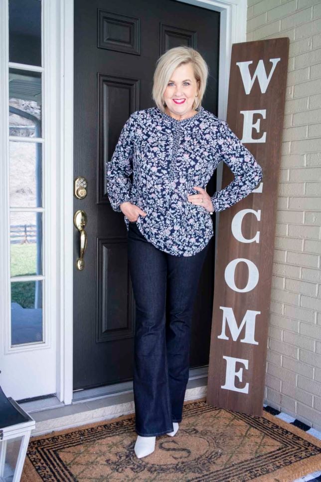 Fashion Blogger 50 Is Not Old is wearing a navy floral tunic, dark wash flare jeans, and white ankle boots
