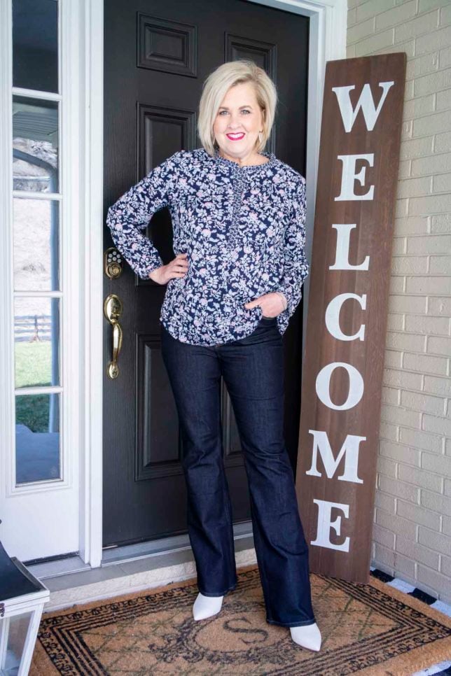 Fashion Blogger 50 Is Not Old is wearing a floral tunic, dark wash skinny flare jeans, and white ankle boots