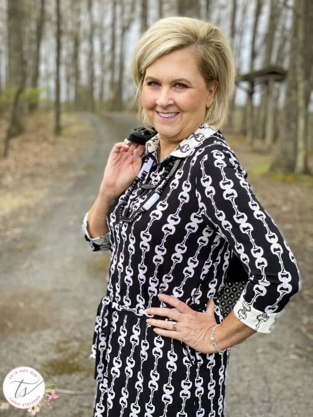 Fashion Blogger 50 Is Not Old is wearing a black and white bit and bridle dress with a black jacket thrown over her shoulder