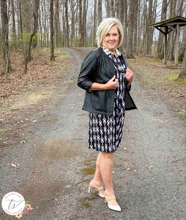 Fashion Blogger 50 Is Not Old is wearing a black and white bit and bridle dress with a black front zip jacket and Rockport heels
