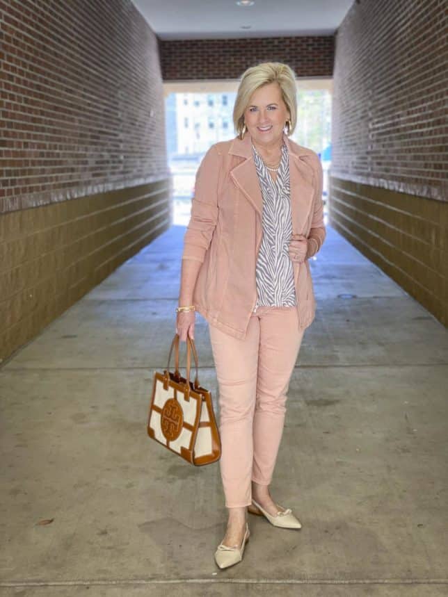 Fashion Blogger 50 Is Not Old is wearing a zebra print top with a pair of blush jeggings, a blush moto jacket, and carrying a Tory Burch tote 