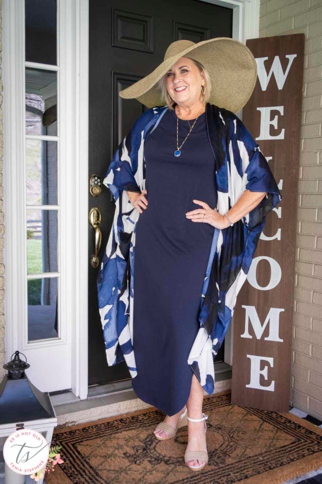 Fashion Blogger 50 Is Not Old is wearing a navy t-shirt dress with gold jewelry, a printed duster, and an oversized straw hat