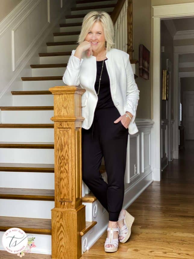 Fashion Blogger 50 Is Not Old is standing by a step of stairs wearing a one and done jumpsuit with a white notched collar blazer
