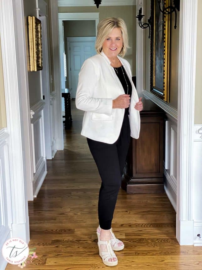 Fashion Blogger 50 Is Not Old is wearing a black jumpsuit, a white notched collar blazer from Gibsonlook, and Michael Kors wedges