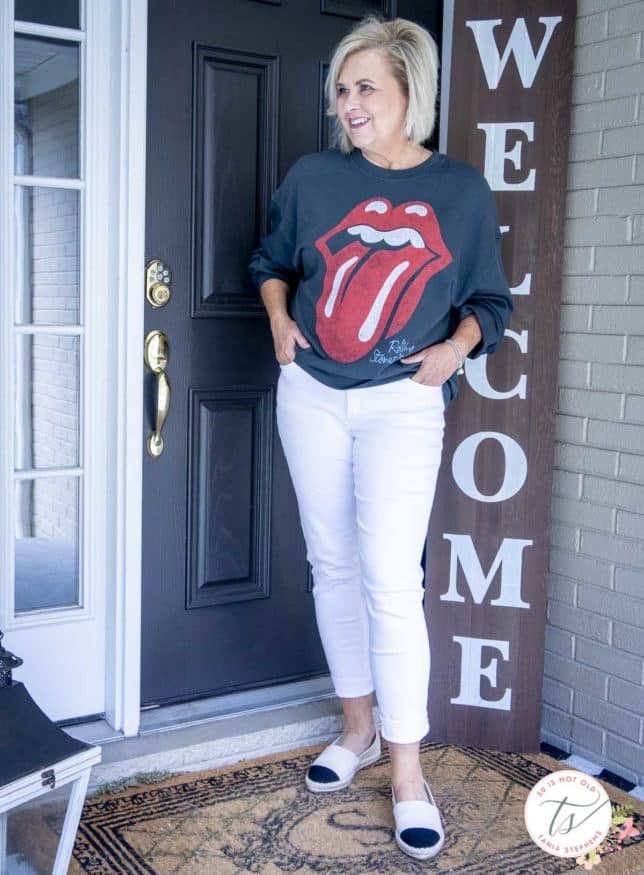 Fashion Blogger 50 Is Not Old is wearing a Rolling Stones sweatshirt with white skinny jeans and white shoes with colored toes
