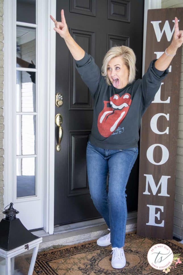 Fashion Blogger 50 Is Not Old is sticking out her tongue while wearing a black Rolling Stones tongue sweatshirt and a pair of jeans