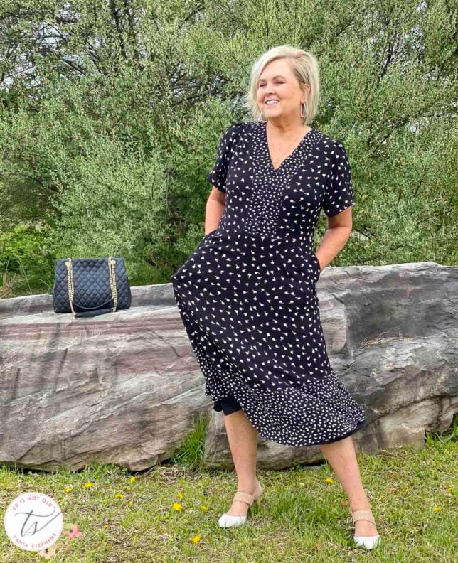 Fashion Blogger 50 Is Not Old is wearing a black and white print dress with beige and white heels and is standing in front of a large rock