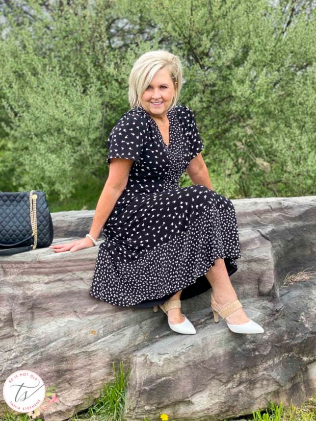 Fashion Blogger 50 Is Not Old is wearing a black and white print dress from Talbots with beige and white heels and is sitting on a rock