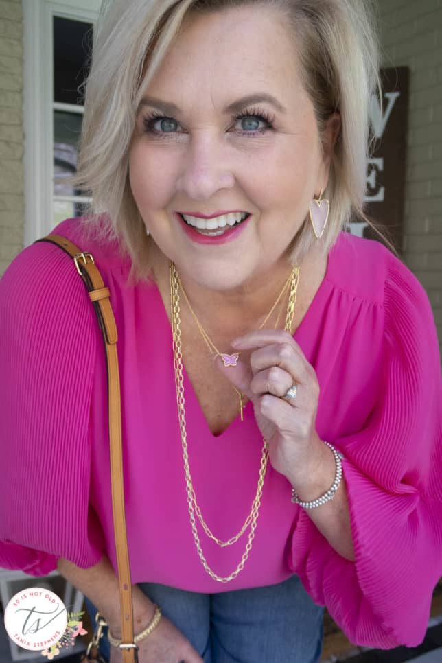 Fashion Blogger 50 Is Not Old is wearing gold jewelry by Kendra Scott with a bright pink blouse