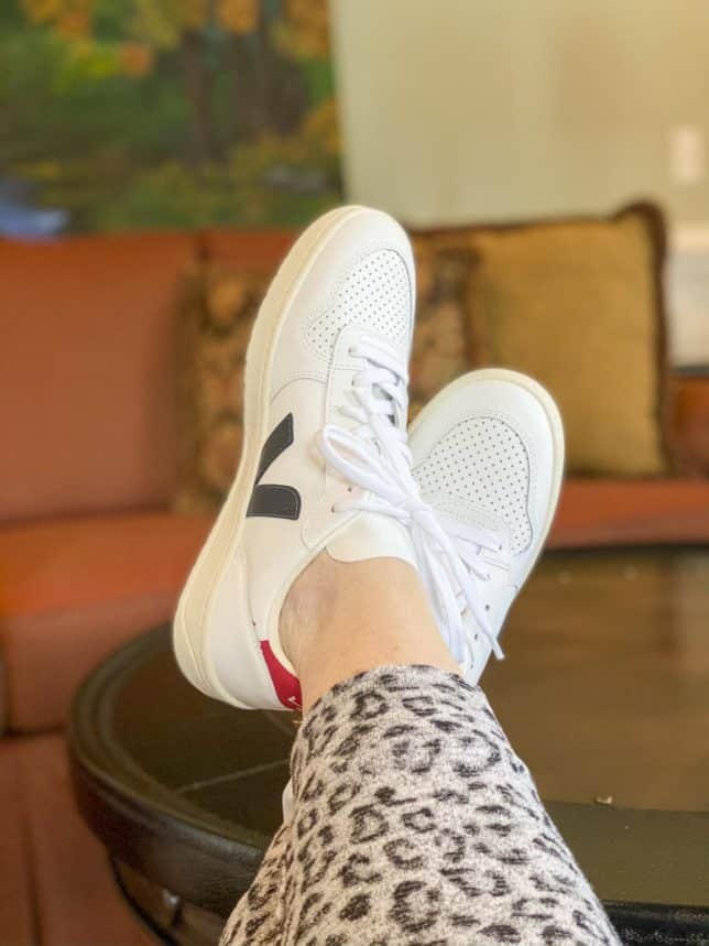 Fashion Blogger 50 Is Not Old is trying on a pair of Veja white sneakers with a navy V and red backs for summer