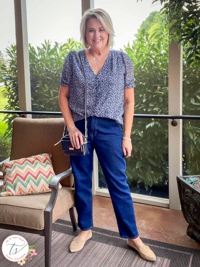 Fashion Blogger 50 Is Not Old is standing in a sunporch wearing a blue and white print blouse and a pair of dark wash jeans