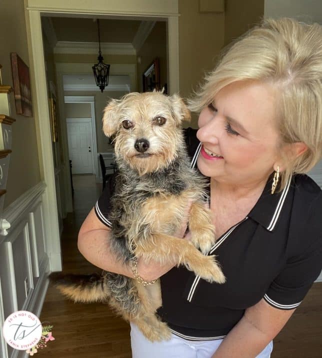 Fashion Blogger 50 Is Not Old is wearing a black polo sweater and holding her dog