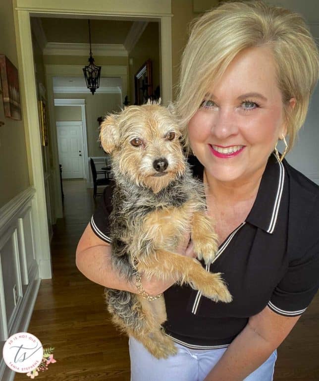 Fashion Blogger 50 Is Not Old is holding her dog while wearing a black polo sweater