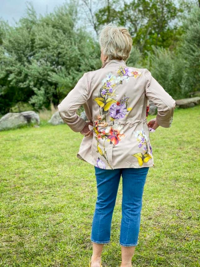 Fashion Blogger 50 Is Not Old is showing the back of a floral satin utility jacket from Chicos