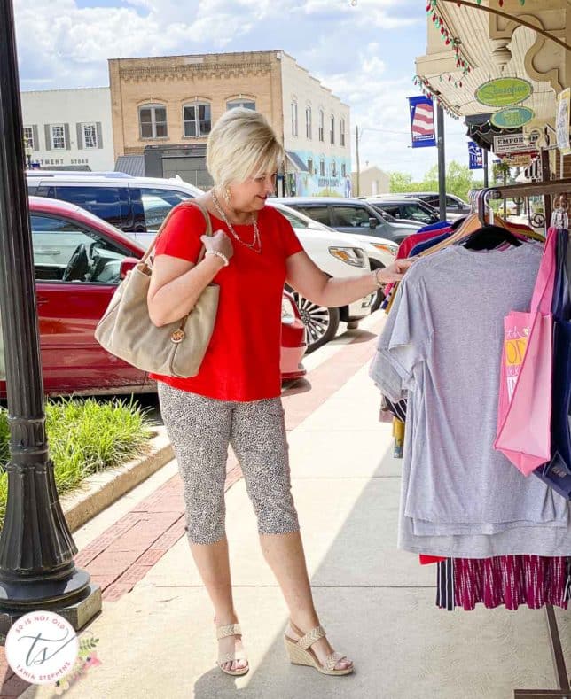 Fashion Blogger 50 Is Not Old is shopping in a red top, animal print capri pants, and a Michael Kors tote bag