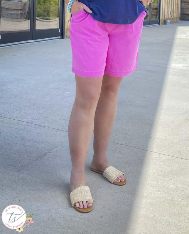Fashion Blogger 50 Is Not Old is wearing a pair of bright pink shorts, and raffia slide sandals