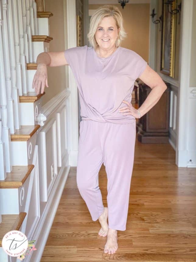 Fashion Blogger 50 Is Not Old is wearing a front twist top and cropped pants in light grape while leaning on a step of stairs