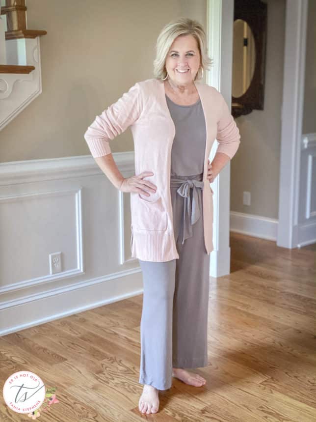Fashion Blogger 50 Is Not Old is wearing a gray jumpsuit with an elastic waist and sash with a pink cardigan