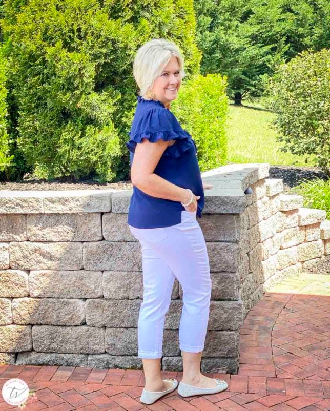 Fashion Blogger 50 Is Not Old is showing the back of a navy ruffle v-neck top with white denim crops