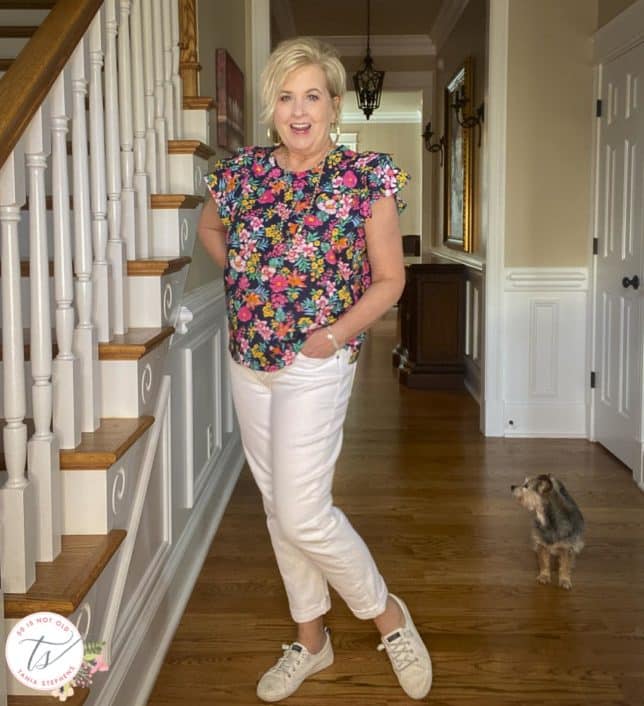 Fashion Blogger 50 Is Not Old is wearing a colorful floral top with ruffled sleeves with a pair of white boyfriend jeans