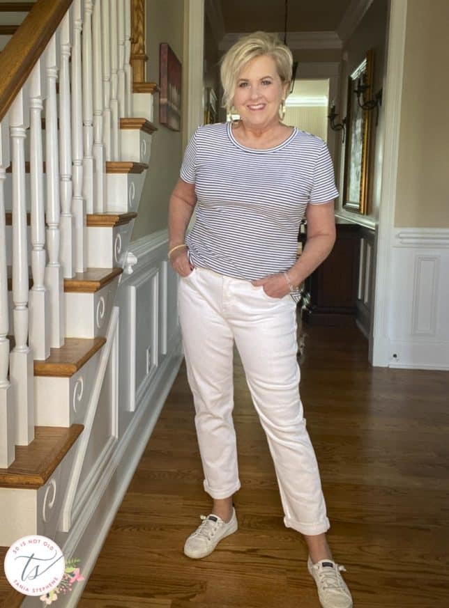 Fashion Blogger 50 Is Not Old is wearing a blue and white striped tee with white boyfriend jeans and white sneakers