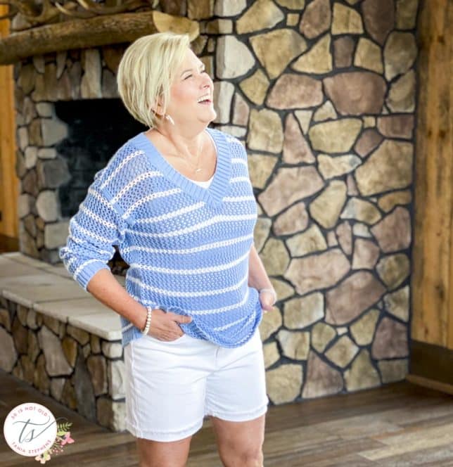 Fashion Blogger 50 Is Not Old is laughing while wearing a blue and white striped mesh sweater with white denim shorts
