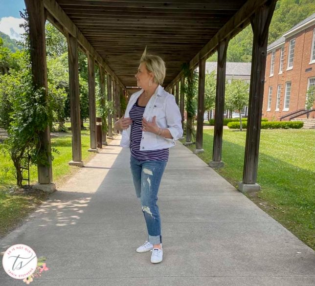 Fashion Blogger 50 Is Not Old is wearing a white denim jacket, a navy and white striped tank top, distressed jeans, and Sperry white sneakers
