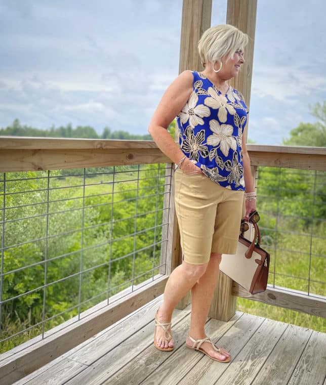 Fashion Blogger 50 Is Not Old is wearing a big, bold blue print sleeveless tank and Bermuda khaki shorts with gold braided sandals