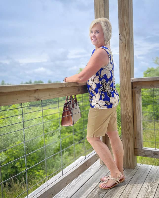 Fashion Blogger 50 Is Not Old is showing the side view of a big, bold blue print sleeveless tank and 10" khaki shorts with gold braided sandals