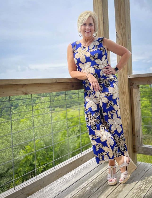 Fashion Blogger 50 Is Not Old is leaning on a rail and wearing a big, bold blue print tank and matching crop pants with espadrille wedge shoes
