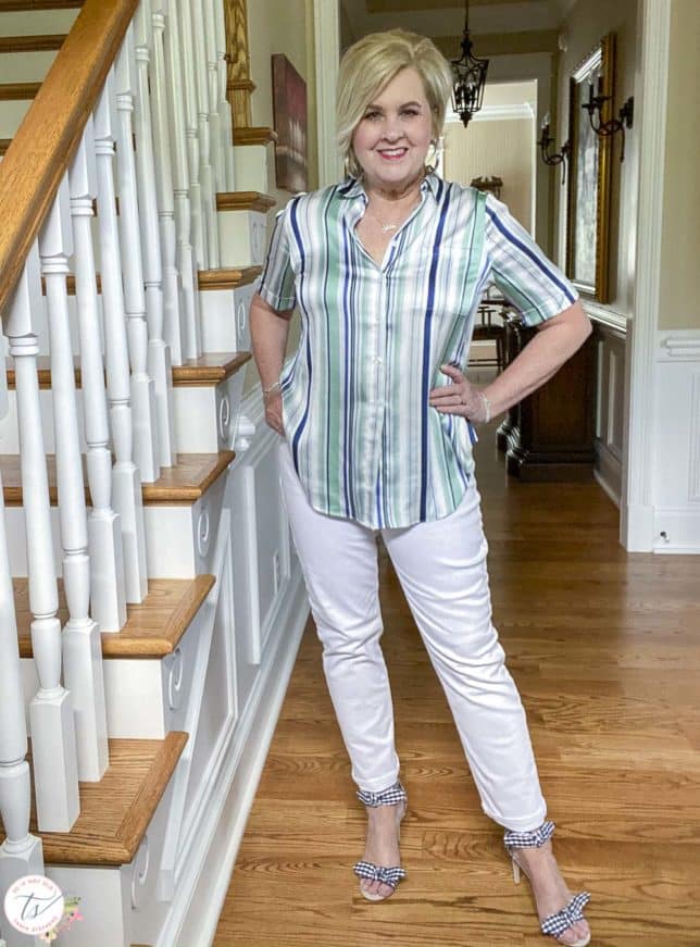 Fashion Blogger 50 Is Not Old is has her hands on her hips while wearing a striped top with white jeans and navy and white gingham heels