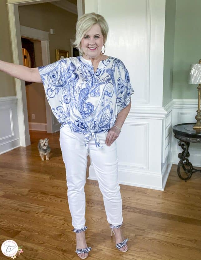 Fashion Blogger 50 Is Not Old is showing the sleeves of a navy and white paisley tie-front top with white jeans and navy and white gingham heels