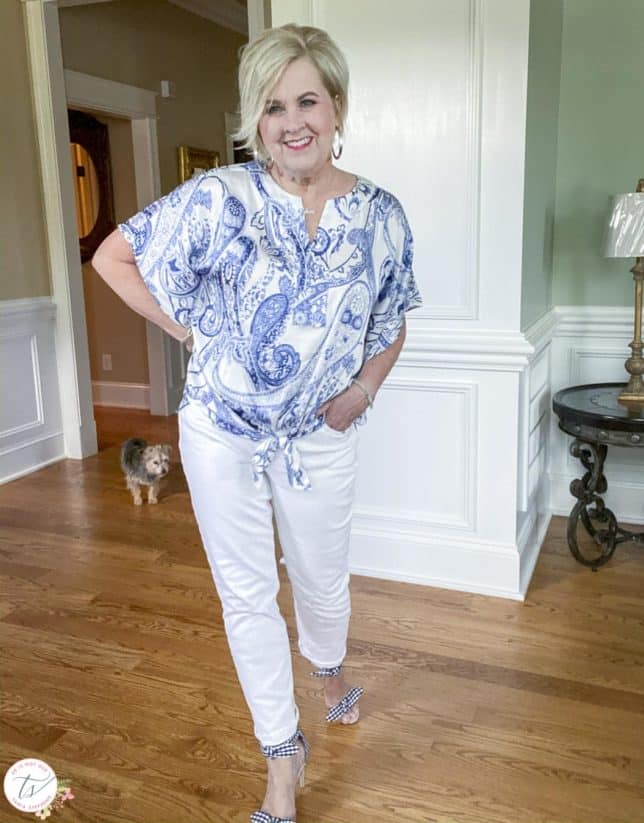 Fashion Blogger 50 Is Not Old is wearing a navy and white paisley tie-front top with white jeans and navy and white gingham heels with a dog in the background