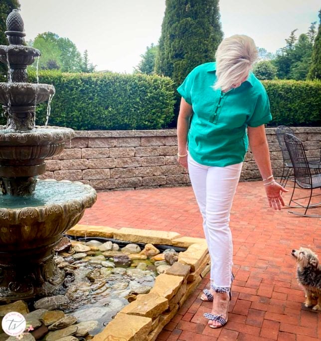 Fashion Blogger 50 Is Not Old is wearing a jade linen pullover shirt with white crop jeans and navy and white gingham heels and petting a dog