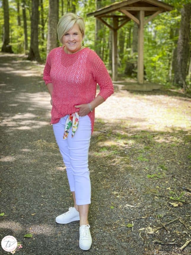 Fashion Blogger 50 Is Not Old is wearing a coral open weave sweater, white cropped jeans with a scarf for the belt, and Keds sneakers