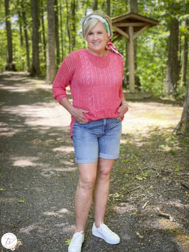 Fashion Blogger 50 Is Not Old is wearing a coral open weave sweater, Bermuda jean shorts, a scarf in her hair, and Keds sneakers