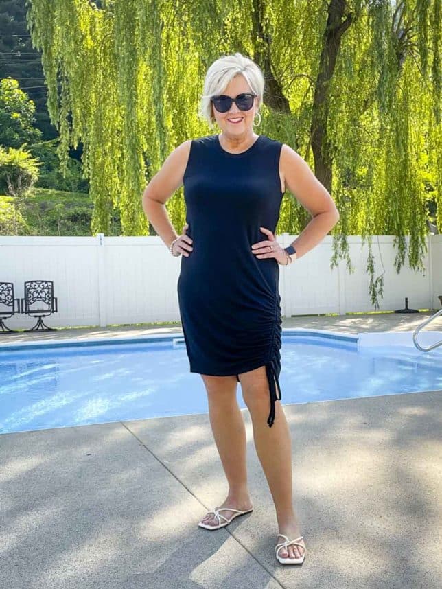 Fashion Blogger 50 Is Not Old is wearing a black ruched dress with black sunglasses and white sandals