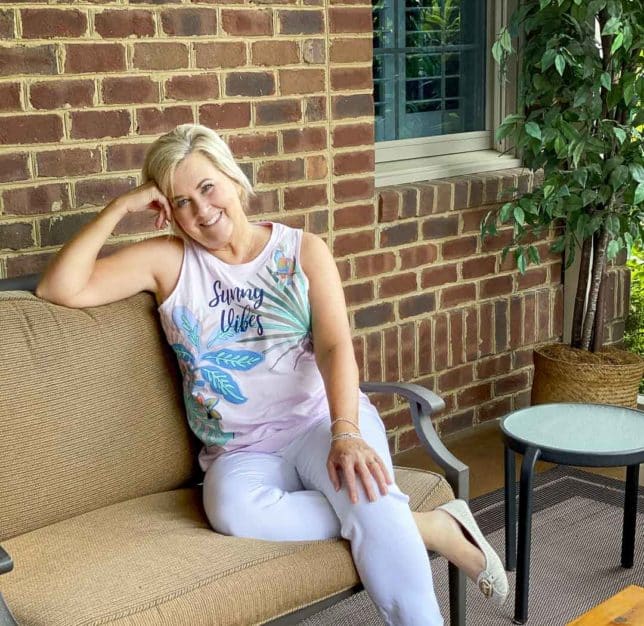 Fashion Blogger 50 Is Not Old is smiling while wearing a pajama tank from Vera Bradley with a pair of white pants