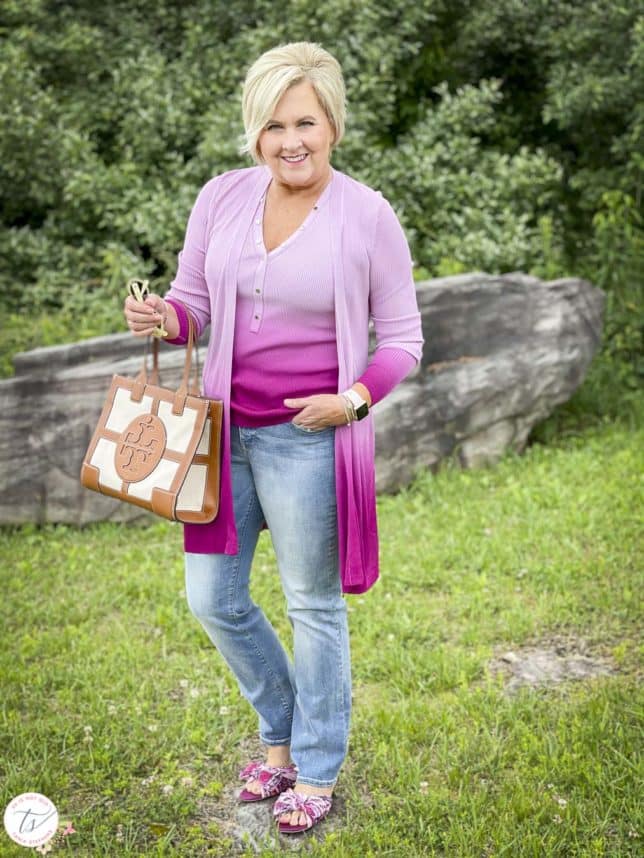 Fashion Blogger 50 Is Not Old is looking colorful in a pink ombre tank and matching coverup, bootcut jeans, pink floral slides, and is carrying a Tory Burch satchel