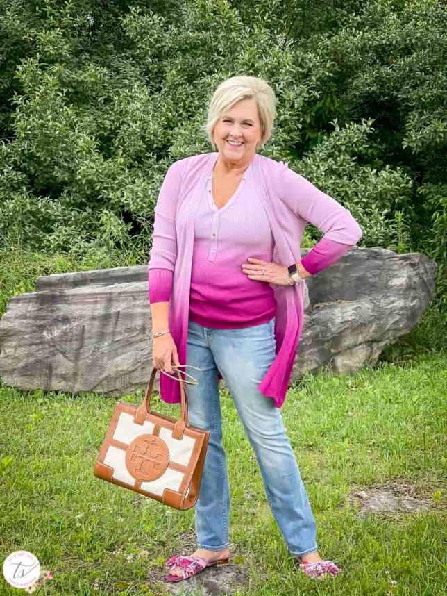 Fashion Blogger 50 Is Not Old is looking colorful in a pink ombre tank and matching coverup, bootcut jeans, pink floral slides, and a Tory Burch satchel