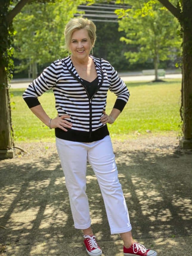 Fashion Blogger 50 Is Not Old is looking sporty and casual in a black and white striped sweater hoodie, white jeans, and red sneakers