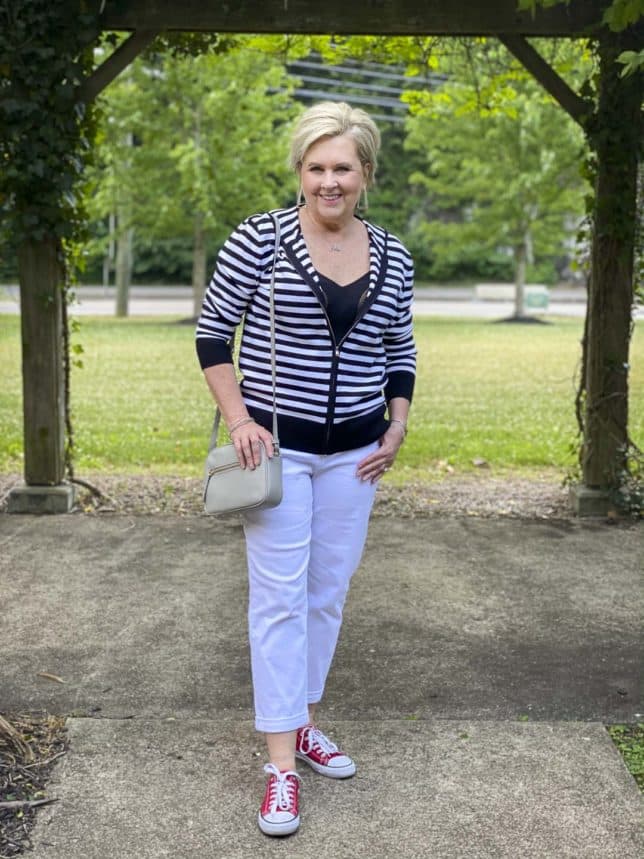Fashion Blogger 50 Is Not Old is looking sporty and casual in a black and white striped zip up sweater hoodie, white jeans, and red sneakers