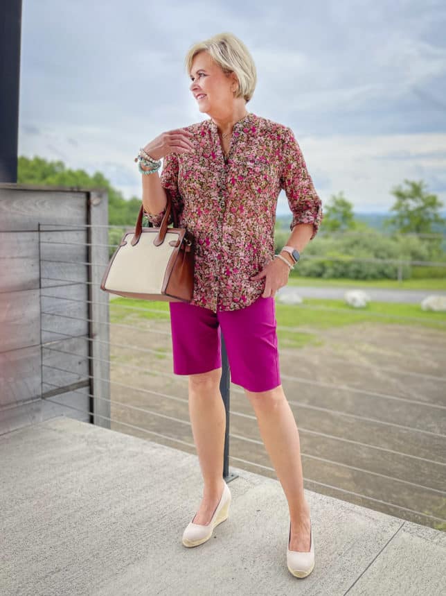 Fashion Blogger 50 Is Not Old is wearing a floral button-up blouse with orchid Bermuda shorts from White House Black Market, neutral wedge espadrilles, and a canvas handbag