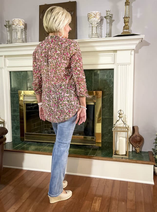 Fashion Blogger 50 Is Not Old is showing the back of a floral button-up blouse with bootcut jeans and neutral wedge espadrilles
